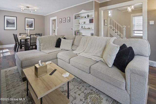 living room featuring an inviting chandelier, stairs, baseboards, wood finished floors, and ornamental molding