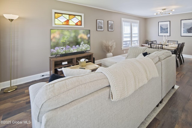 living area featuring an inviting chandelier, baseboards, ornamental molding, and dark wood-style floors