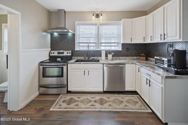 kitchen featuring wall chimney range hood, white cabinets, appliances with stainless steel finishes, and a sink