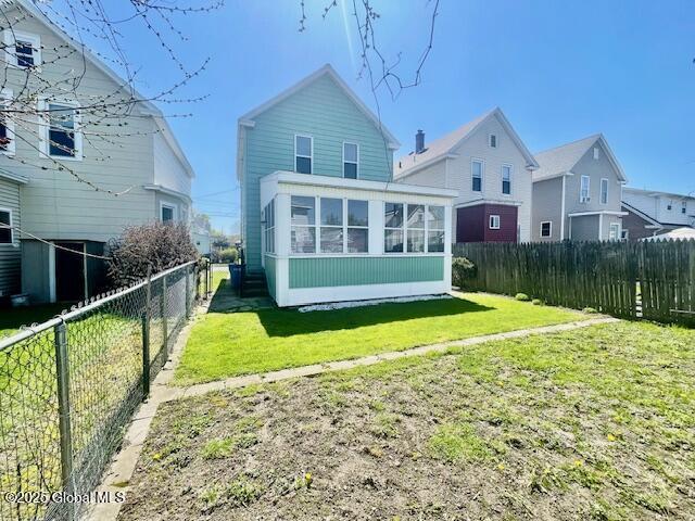 rear view of property featuring a sunroom, a fenced backyard, and a yard