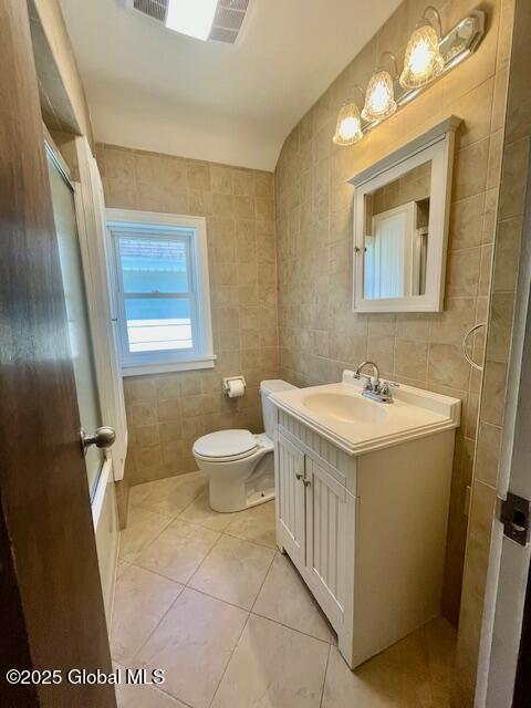 bathroom with tile walls, tile patterned flooring, vanity, and toilet