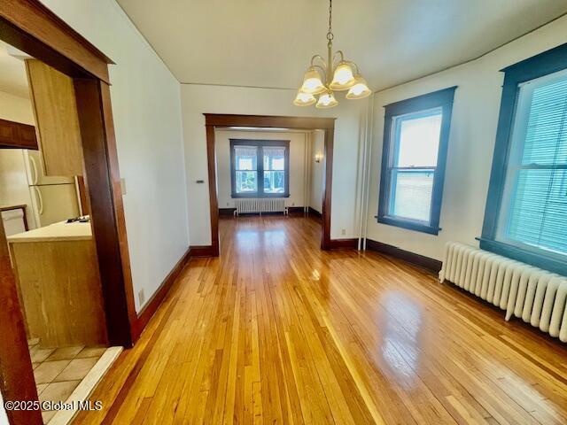 unfurnished dining area with radiator heating unit, baseboards, light wood-style floors, and a notable chandelier