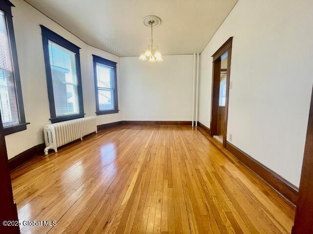 unfurnished dining area featuring radiator heating unit, baseboards, light wood finished floors, and a notable chandelier