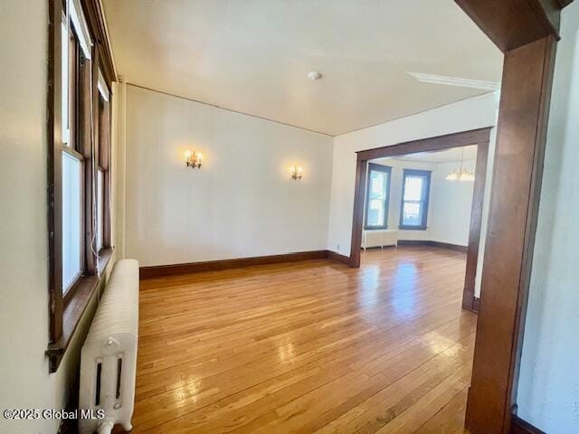 empty room featuring baseboards, a notable chandelier, radiator heating unit, and wood finished floors