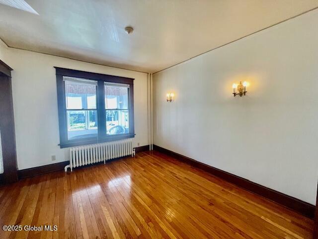 unfurnished room with baseboards, radiator, a chandelier, and hardwood / wood-style floors