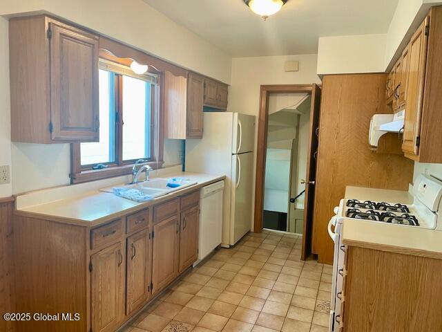 kitchen with light tile patterned flooring, white appliances, extractor fan, light countertops, and a sink