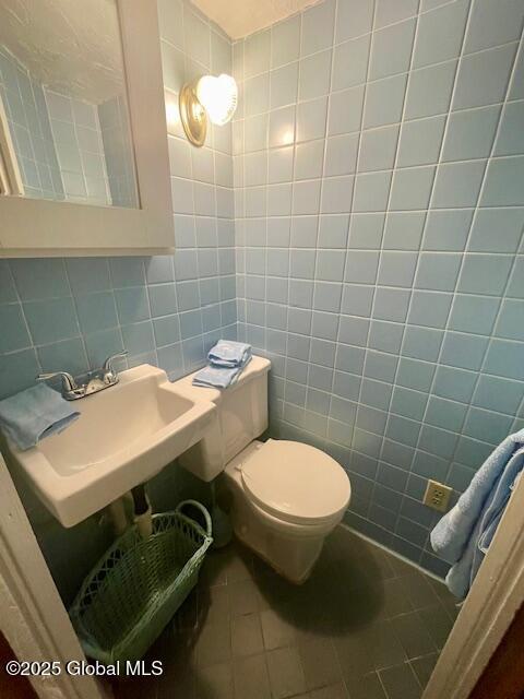 half bath featuring a sink, tile walls, toilet, and tile patterned floors