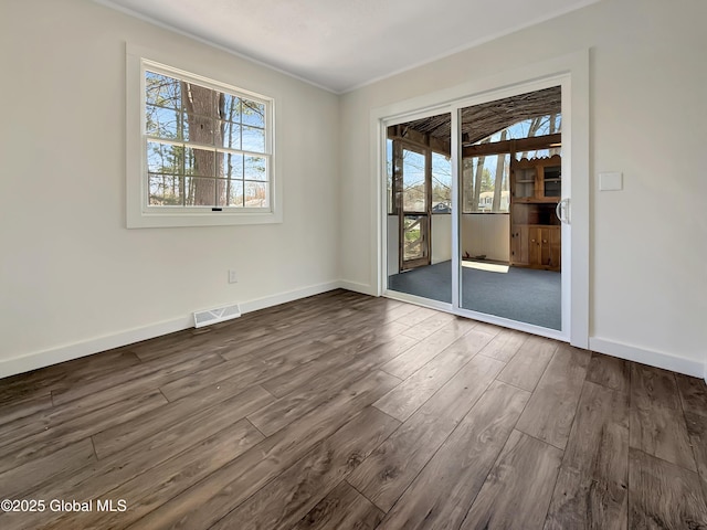unfurnished room featuring visible vents, ornamental molding, dark wood finished floors, and baseboards
