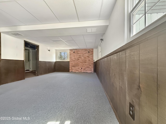basement with a wainscoted wall, wood walls, carpet floors, and visible vents
