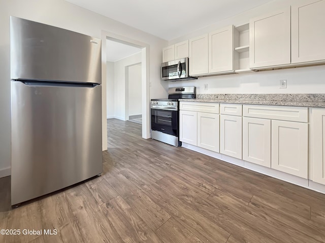 kitchen with appliances with stainless steel finishes, open shelves, wood finished floors, light stone counters, and white cabinetry