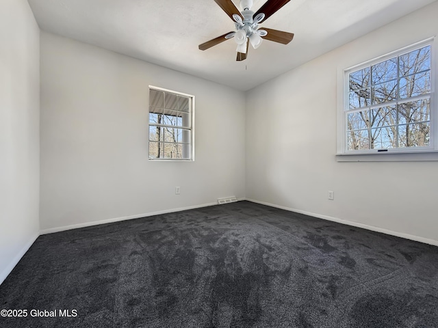 empty room featuring dark colored carpet, a ceiling fan, and baseboards