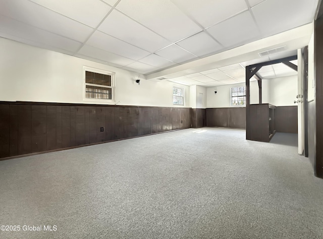 basement with wooden walls, wainscoting, a drop ceiling, and visible vents