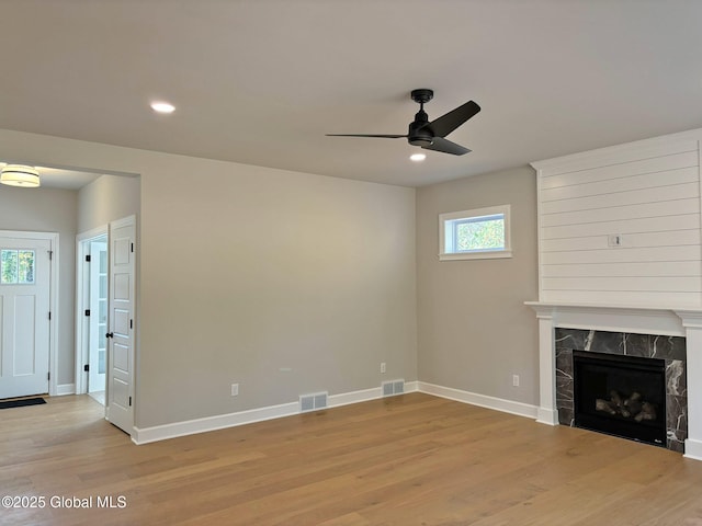 unfurnished living room with ceiling fan, visible vents, a high end fireplace, baseboards, and light wood-style floors
