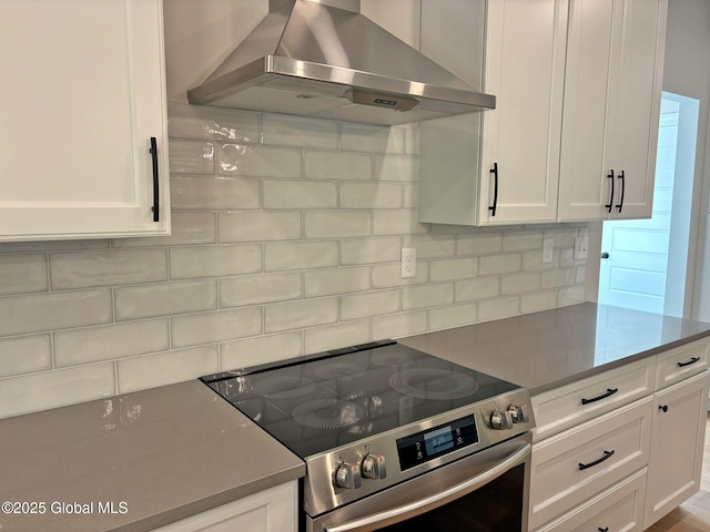 kitchen with decorative backsplash, white cabinets, wall chimney range hood, and stainless steel electric range oven