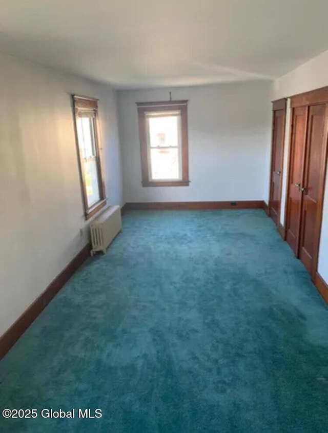 unfurnished bedroom featuring baseboards, radiator, and carpet