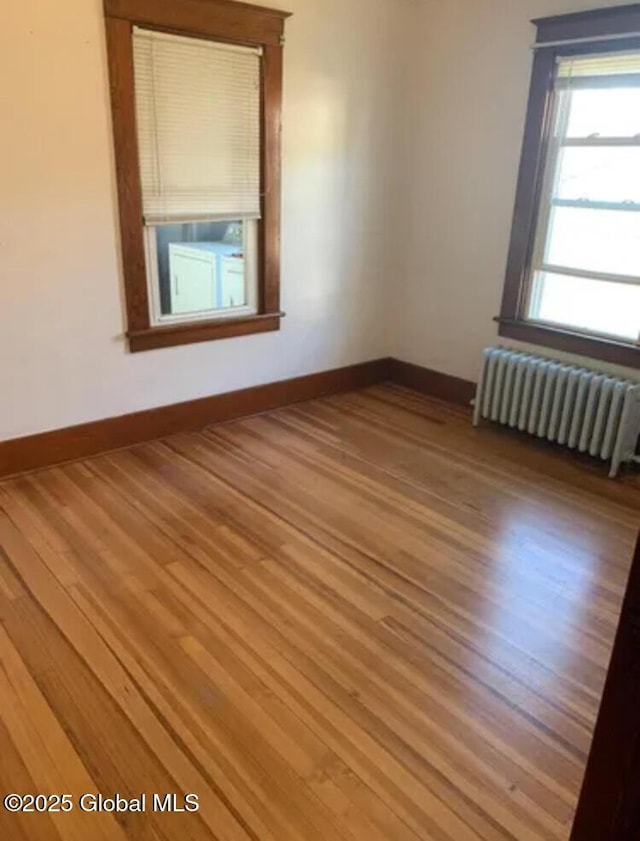 spare room featuring baseboards, radiator heating unit, and light wood-style flooring