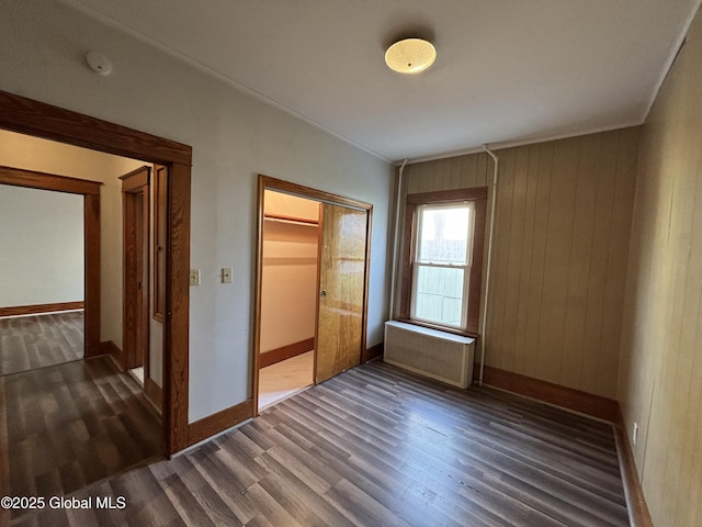 unfurnished bedroom with crown molding, a closet, baseboards, radiator, and dark wood-type flooring