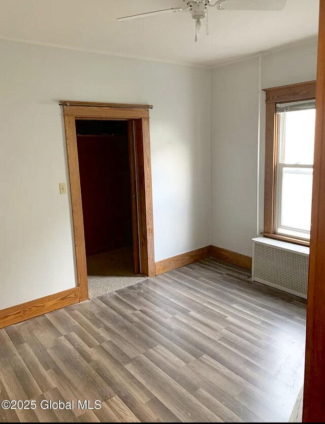 spare room featuring baseboards, radiator, a ceiling fan, and wood finished floors