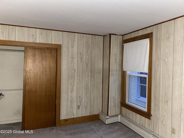 interior space with wooden walls, a baseboard heating unit, a closet, and carpet flooring