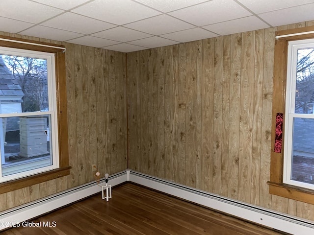 unfurnished room with wood walls, a baseboard heating unit, a paneled ceiling, and dark wood-style floors