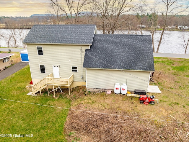 rear view of house with a water view, a yard, and a shingled roof