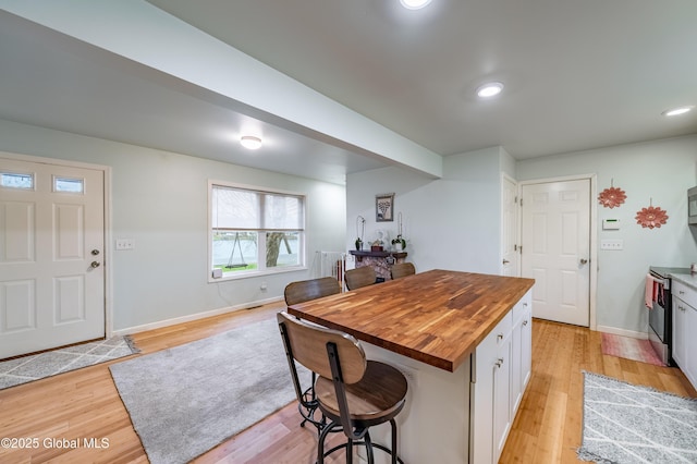 kitchen with wood counters, light wood-type flooring, a breakfast bar area, appliances with stainless steel finishes, and white cabinetry