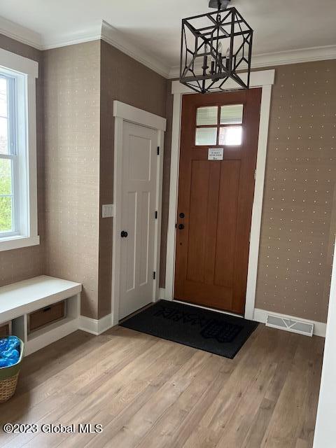 entryway featuring baseboards, ornamental molding, an inviting chandelier, and light wood-style floors