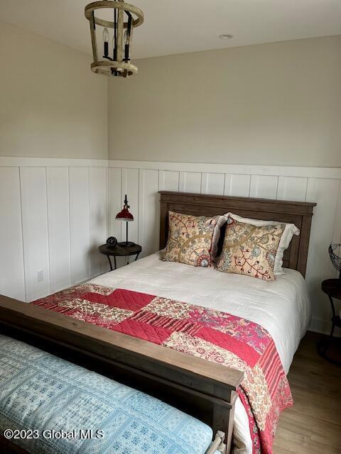 bedroom with wood finished floors, a decorative wall, and a wainscoted wall