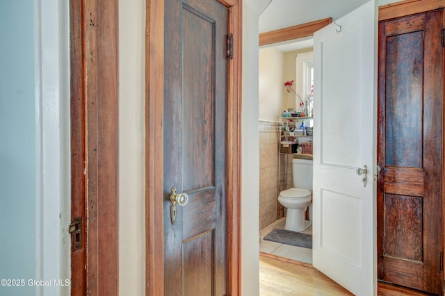 bathroom with toilet, a wainscoted wall, tile walls, and wood finished floors