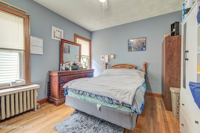 bedroom featuring radiator heating unit, wood finished floors, baseboards, and multiple windows