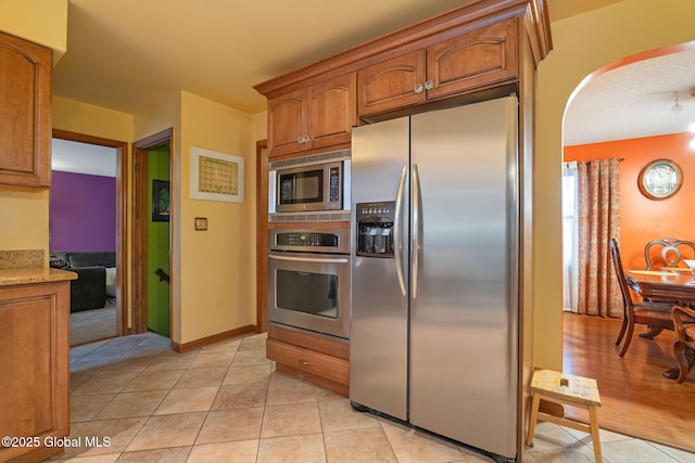 63 Pawling Ave, Mechanicville, NY 12118 - kitchen with brown cabinets, appliances with stainless steel finishes, arched walkways, light tile patterned flooring, and light stone countertops