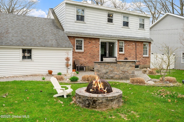 back of house featuring a yard, brick siding, a fire pit, and a shingled roof