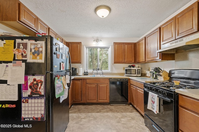 kitchen with brown cabinets, a sink, light countertops, under cabinet range hood, and black appliances