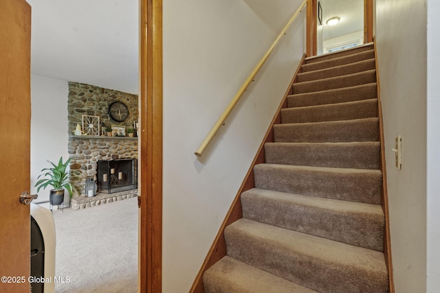 stairway with a stone fireplace and carpet