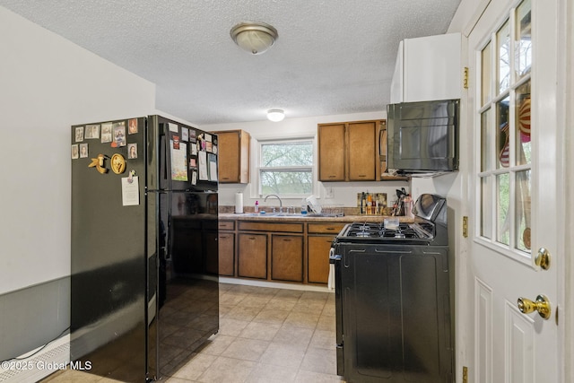kitchen with a textured ceiling, brown cabinets, a sink, light tile patterned floors, and black appliances