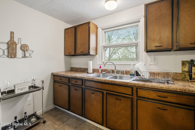 kitchen featuring a textured ceiling, brown cabinetry, and a sink