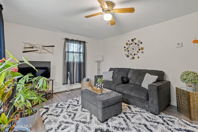 living area featuring a textured ceiling, ceiling fan, baseboards, and wood finished floors