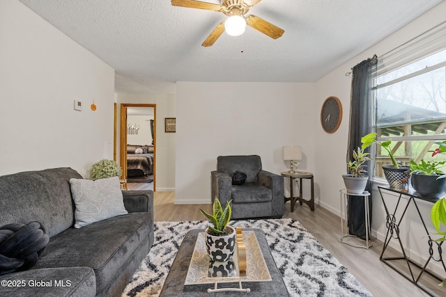 living room with baseboards, a ceiling fan, light wood finished floors, and a textured ceiling