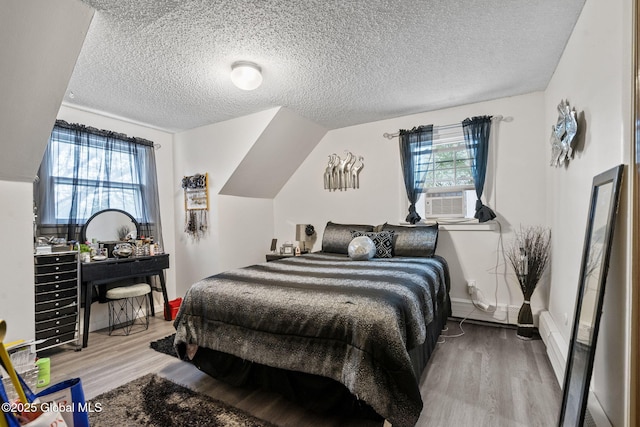 bedroom with a textured ceiling, multiple windows, wood finished floors, and cooling unit