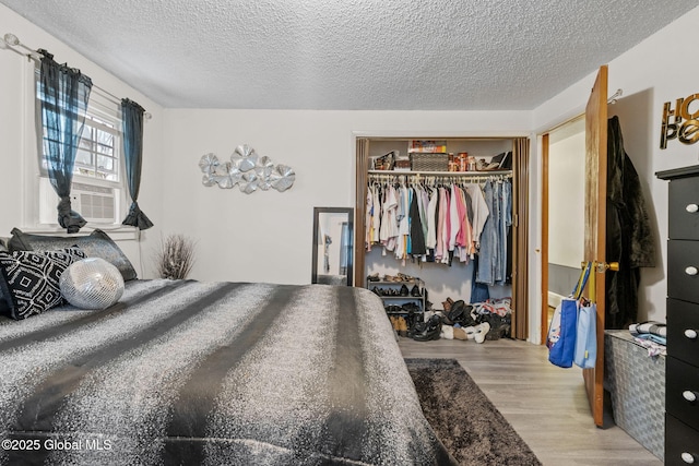 bedroom with a textured ceiling, cooling unit, a closet, and wood finished floors