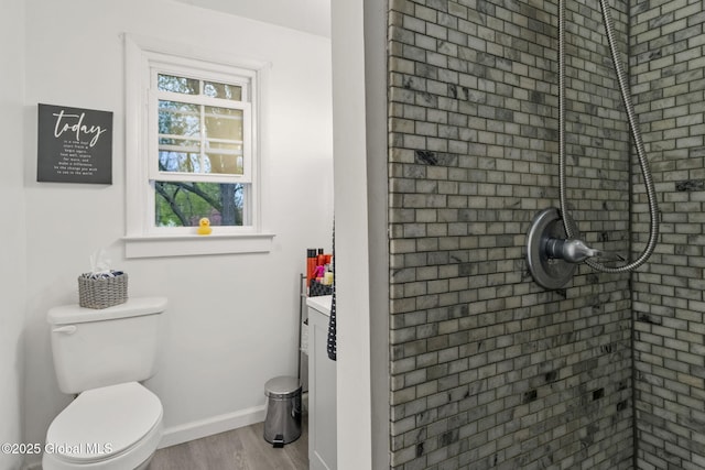 full bath featuring toilet, baseboards, tiled shower, and wood finished floors