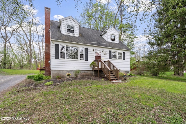 new england style home with roof with shingles, a chimney, and a front yard