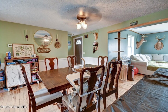 dining room featuring light wood-style floors, a textured ceiling, and a wainscoted wall