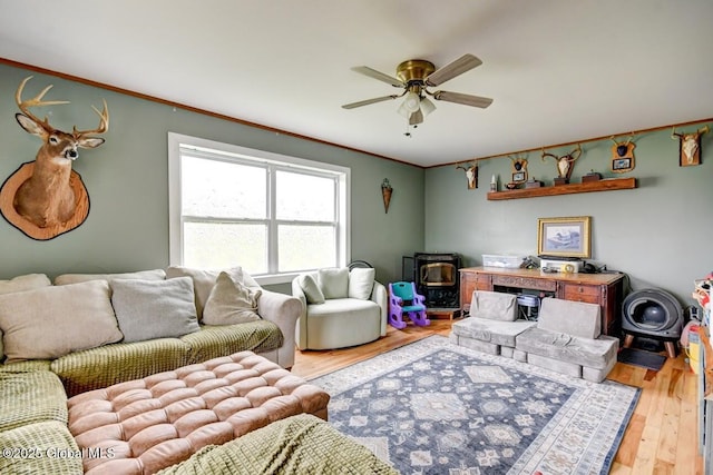 living area featuring crown molding, a wood stove, ceiling fan, and wood finished floors