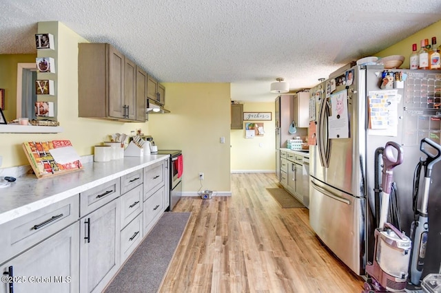kitchen with light wood-type flooring, light countertops, a textured ceiling, under cabinet range hood, and stainless steel appliances