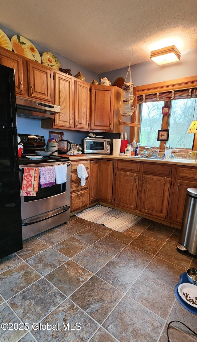 kitchen featuring stone tile floors, a textured ceiling, stainless steel range with electric stovetop, freestanding refrigerator, and under cabinet range hood