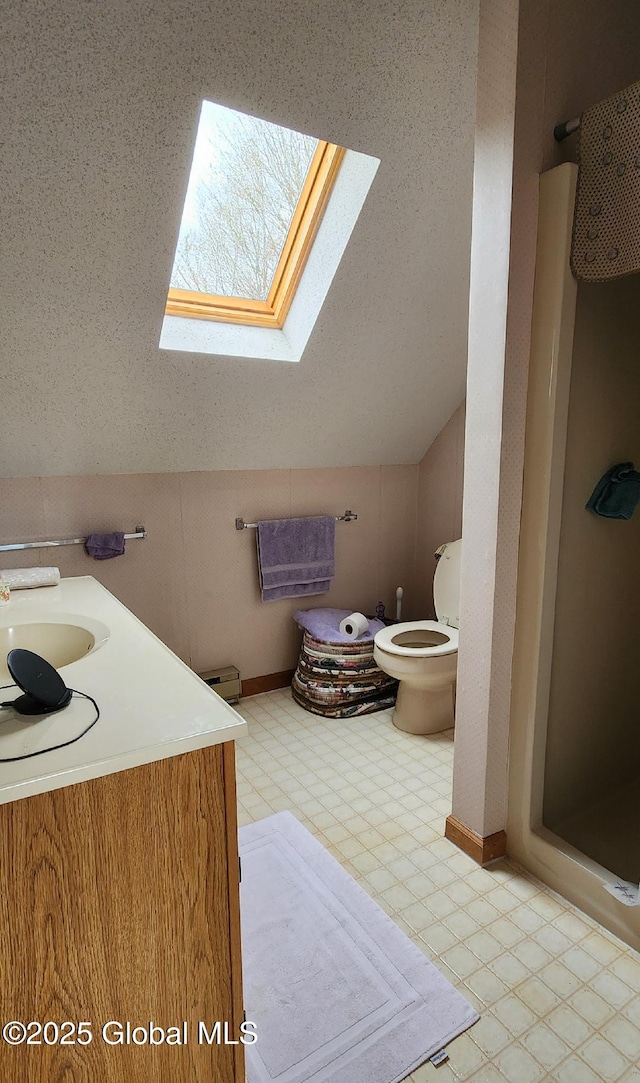 bathroom with vaulted ceiling with skylight, tile patterned floors, toilet, a sink, and a stall shower