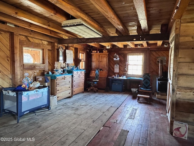 miscellaneous room with wooden walls, a wood stove, beamed ceiling, and hardwood / wood-style flooring