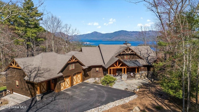 chalet / cabin featuring a mountain view, roof with shingles, a chimney, and aphalt driveway