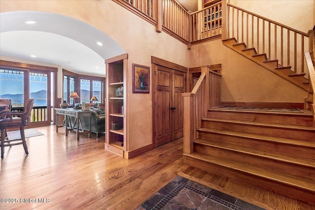 stairs featuring wood finished floors, arched walkways, and recessed lighting